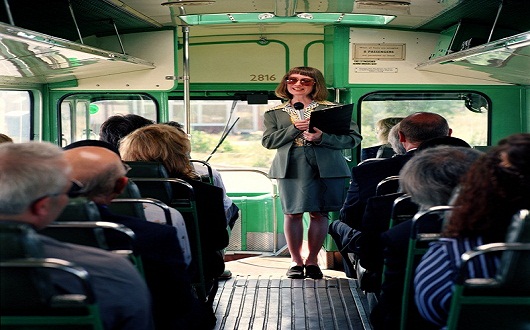 Female tour guide with microphone and clipboard on packed bus