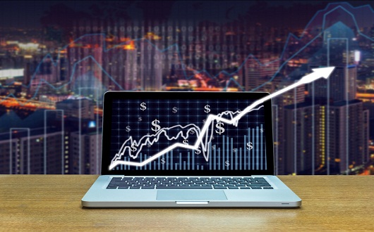 Stock exchange market trading graph over the screen of computer laptop on wood table over the photo blurred of trading graph background, business marketing trade concept