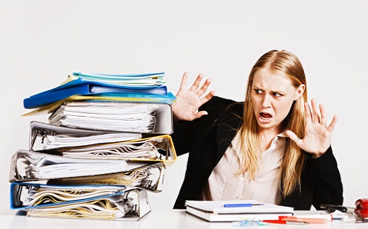 Frightened young businesswoman recoils from towering pile of work