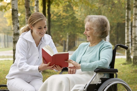 Caregiver reading to woman in wheelchair