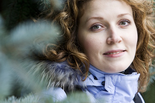 Beautiful young woman and blurred fir branch on foreground