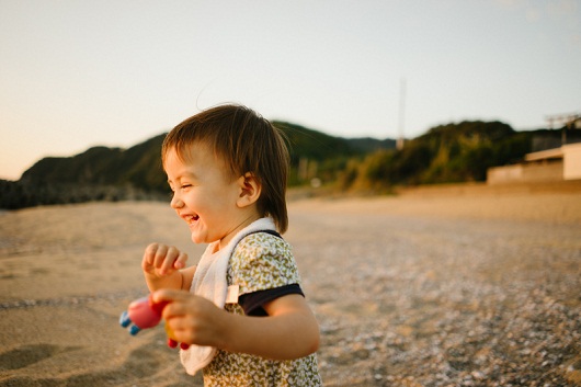 1 year old baby girl laughing and playing on a beach during sunset with toy in hand.